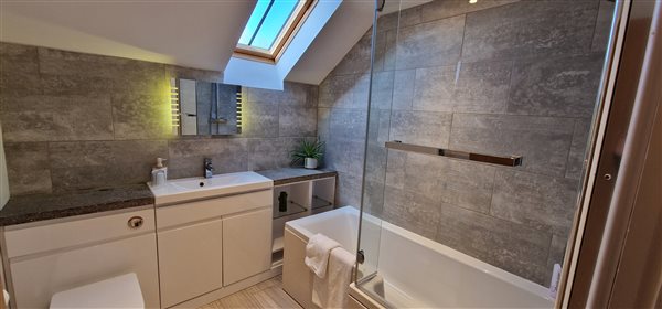 main bathroom with basin, bath with shower over, toilet and vanity mirror with lights