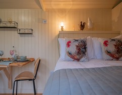 Cosy glamping hut interior with a neatly made bed and small dining table.