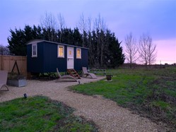 Shepherd’s hut in a rural field at sunset with outdoor seating.