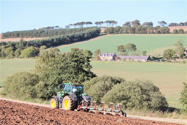 Tractor ploughing with cottages in backdrop