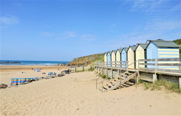 Summerleaze beach in Bude, sandy beach with beach huts on the right and wind breaks on the sand
