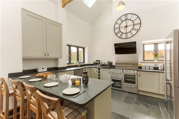 Large sage coloured kitchen with breakfast bar. Slate floor and worktop with stainless steel range style cooker and dishwasher