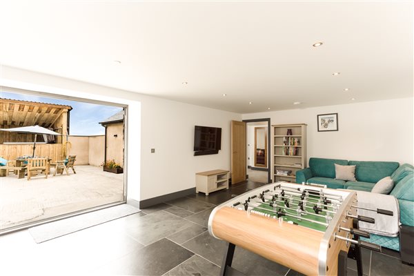 2nd lounge area with table football, slate floor, large tv, teal corner sofa with bifold doors opening onto the enclosed courtyard