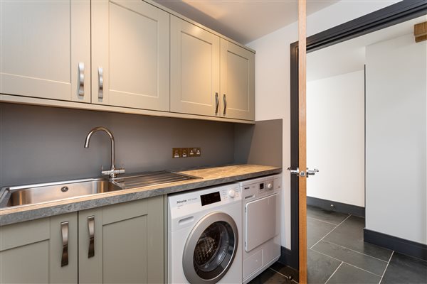 Utility room with washing machine, tumble dryer, sage cabinets and stainless steel sing and tap