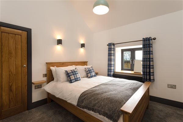 Bedroom with double oak bed, white linen, oak doored built in wardrobe and blue checked curtains. 