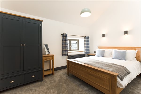 King bedroom with oak framed bed with large blue wardrobe, grey carpet and window overlooking  the courtyard 