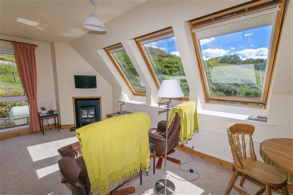 Upstairs lounge in holiday cottage with 3 windows looking onto a hillside