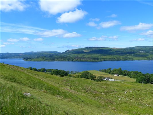 green hillside with 2 cottages a field, water and hills