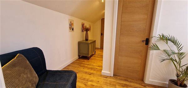 landing space with hallway leading the 3rd bedroom, blue sofa bed (as a chair), plant to the right and a wooden storage chest along the wall