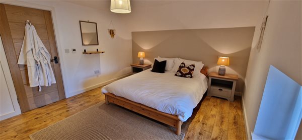 master bedroom with king bed, robes hanging at the door to the left, 2 bedside tables with striped lamps