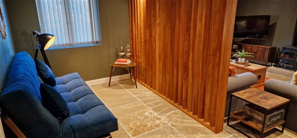 a plush blue sofa bed is on the left. a large lamp and coffee table close by with slatted wooden room divider to the right partially closing off the rest of the living area