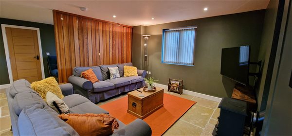 the main living area has two light blue squishy sofas focused around a log burner and tv, behind them a wooden room divider partially encloses the space