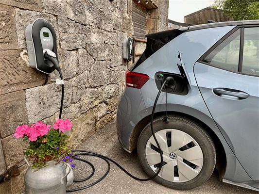 A blue car plugged into an EV charging point on a stone barn wall