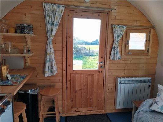 Front door and window of pod showing curtains, radiator, shelfing, worktop and stools Front door and window of pod showing curtains, radiator, shelfing, worktop and stools