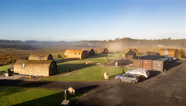 Aerial view of Galloway Retreats luxury glamping pods and cabins in Dumfries and Galloway, Scotland, showing wooden accommodation, landscaped grounds, parking areas and beautiful surrounding 