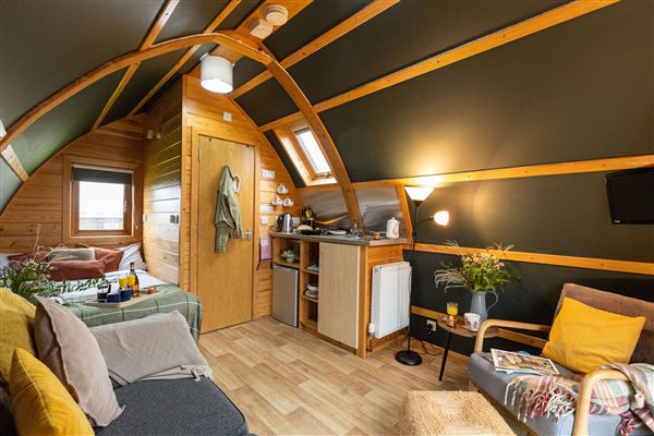 Spacious glamping pod interior at Galloway Retreats in Dumfries and Galloway, Scotland, featuring a cosy sleeping area, comfortable seating, kitchenette, warm wooden beams and stylish furnishings.