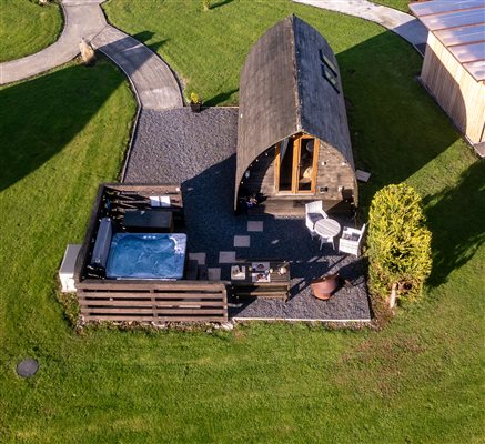 Aerial view of a luxury glamping pod at Galloway Retreats in Dumfries and Galloway, Scotland, featuring a private outdoor hot tub, seating area and surrounding green countryside.