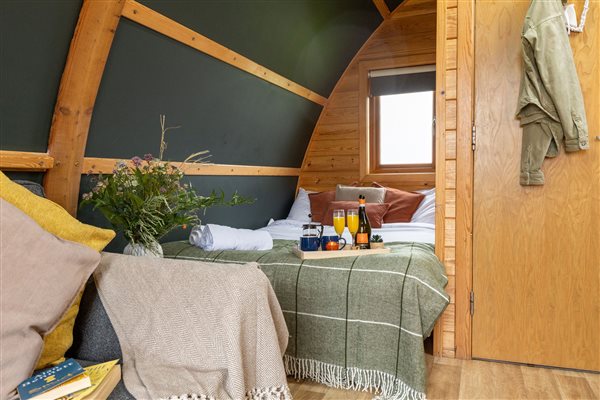 Cosy bedroom in a luxury glamping pod featuring a comfortable bed with soft bedding, warm wooden interiors and a breakfast tray for a relaxing countryside getaway. Cosy bedroom in a luxury glamping pod featuring a comfortable bed with soft bedding, warm wooden interiors and a breakfast tray for a relaxing countryside getaway.