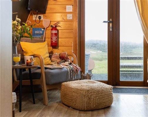 Cosy glamping pod interior at Galloway Retreats in Dumfries and Galloway, Scotland, featuring warm wooden walls, comfortable seating, stylish furnishings and glass doors overlooking the countryside