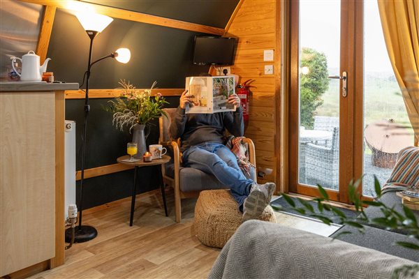Cosy interior of a luxury glamping pod at Galloway Retreats, featuring comfortable seating, warm wooden furnishings, soft lighting and glass doors opening onto the private outdoor area.