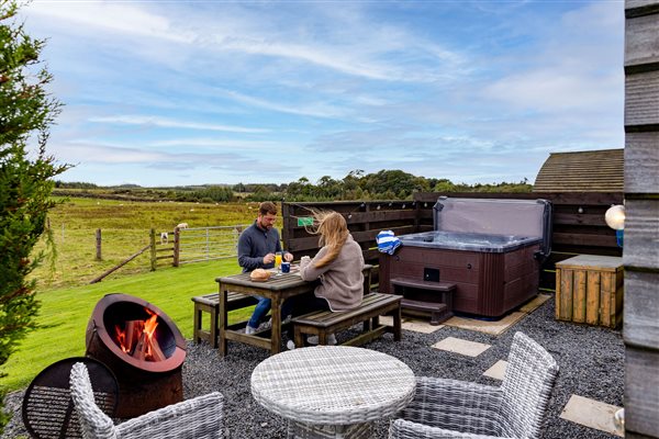 Private outdoor seating and dining area at Galloway Retreats luxury cabins in Dumfries and Galloway, Scotland, featuring a hot tub, cosy fire pit, comfortable garden furniture and beautiful countryside views.