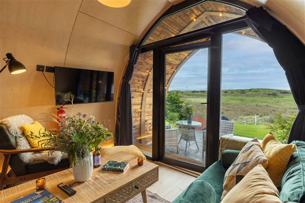 Luxury glamping pod living room with comfortable sofas, panoramic countryside views and large glass doors opening onto a private patio. Luxury glamping pod living room with comfortable sofas, panoramic countryside views and large glass doors opening onto a private patio.