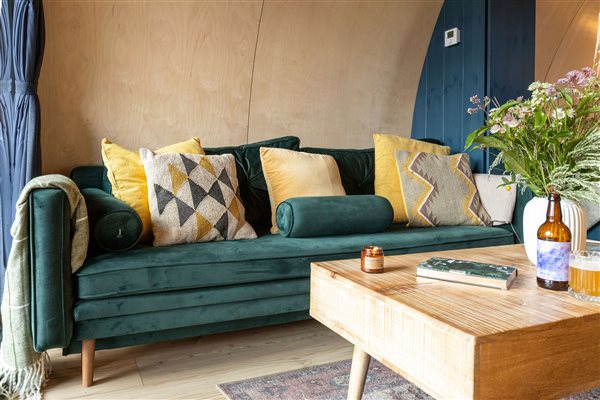 Comfortable living area in a luxury glamping pod featuring a plush green velvet sofa, decorative cushions and a wooden coffee table with flowers. Comfortable living area in a luxury glamping pod featuring a plush green velvet sofa, decorative cushions and a wooden coffee table with flowers.