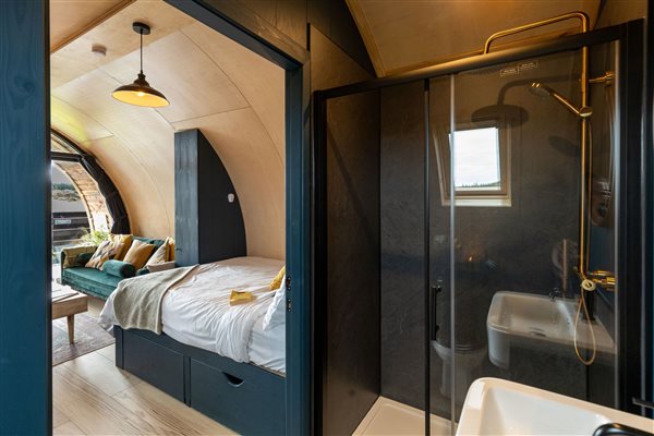 Luxury glamping pod interior at Galloway Retreats featuring a cosy double bed, curved architectural design and modern en-suite bathroom with glass walk-in shower. Luxury glamping pod interior at Galloway Retreats featuring a cosy double bed, curved architectural design and modern en-suite bathroom with glass walk-in shower.
