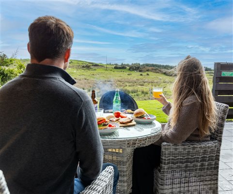 Couple enjoying outdoor dining and drinks on a private patio at Galloway Retreats, overlooking beautiful countryside views. Couple enjoying outdoor dining and drinks on a private patio at Galloway Retreats, overlooking beautiful countryside views.