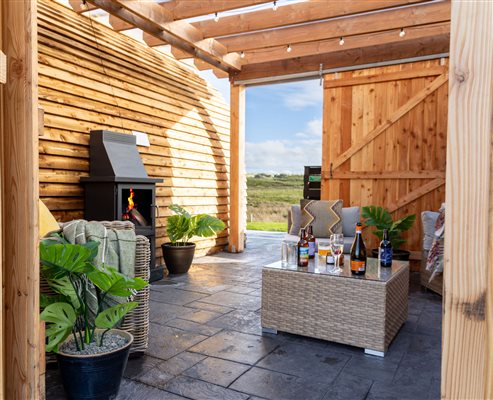 Sheltered outdoor seating area at Galloway Retreats, featuring a cosy fireplace, comfortable garden furniture, timber pergola and countryside views. Sheltered outdoor seating area at Galloway Retreats, featuring a cosy fireplace, comfortable garden furniture, timber pergola and countryside views.