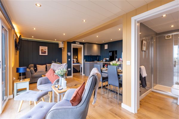 Spacious open-plan living area in a large luxury countryside cabin, featuring comfortable sofas, stylish modern furnishings, a dining area and a fully equipped kitchen.
