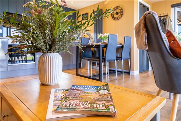 Cosy living and dining area at Galloway Retreats luxury cabins, featuring a wooden coffee table, fresh flowers, comfortable seating and modern dining furniture. Cosy living and dining area at Galloway Retreats luxury cabins, featuring a wooden coffee table, fresh flowers, comfortable seating and modern dining furniture.