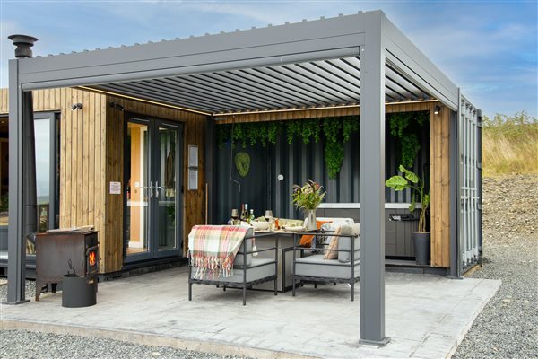 Luxury countryside cabin with a spacious outdoor patio, private hot tub, modern covered pergola, comfortable garden seating and dining area, perfect for relaxing outdoors.