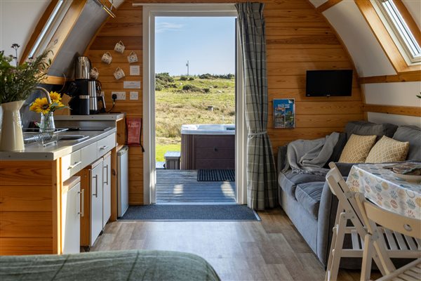 Interior of the Superior Large Stepless Pod at Galloway Retreats in Dumfries and Galloway, featuring a modern kitchenette, cosy seating area, wooden furnishings and glass doors opening onto a private hot tub and beautiful countryside views.
