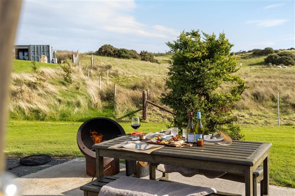 Private outdoor dining area at the Superior Large Stepless Pod at Galloway Retreats in Dumfries and Galloway, Scotland, featuring a wooden dining table, fire pit and beautiful countryside views.