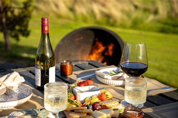 Outdoor dining at Galloway Retreats in Dumfries and Galloway, Scotland, featuring freshly prepared food, a glass of red wine and a cosy wood-fired pizza oven surrounded by beautiful countryside.