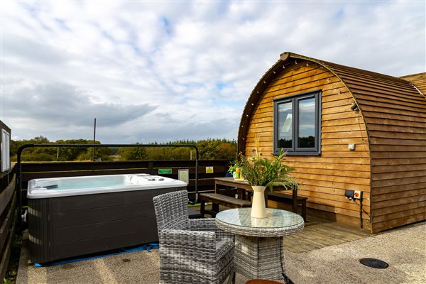 Luxury wooden glamping pod with private outdoor hot tub, patio dining table and wicker chairs, overlooking peaceful countryside. Luxury wooden glamping pod with private outdoor hot tub, patio dining table and wicker chairs, overlooking peaceful countryside.
