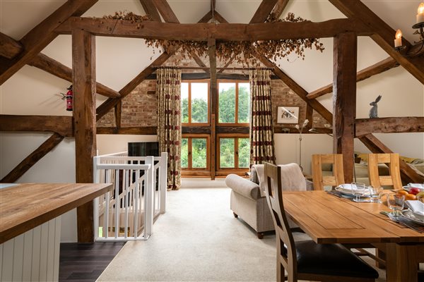 exposed beams and open plan room with high vaulted ceilings, dining table and panoramic windows with garden views