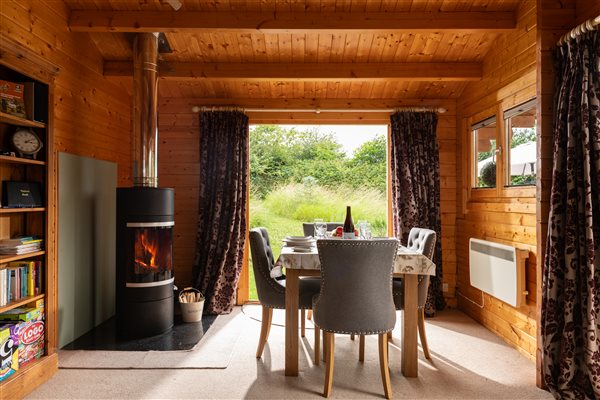 dining table for 4 with comfy chairs and double doors leading to garden and log burner on left side