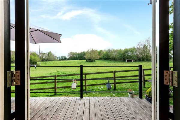 View from inside hut to green field surrounded by woodland trees