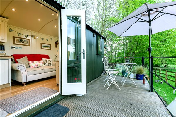 Balcony with seating and sun parasol open double doors from hut looking in to sofa area